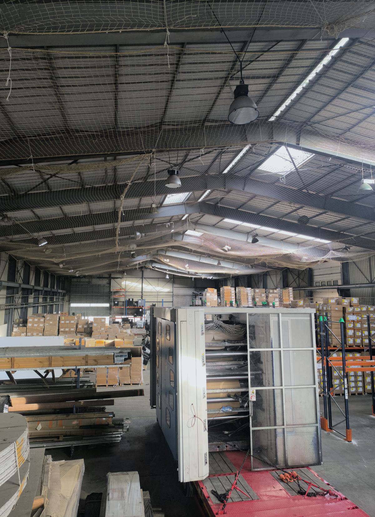 Après : la même halle, filet tendu sur toute la portée, stock et machines en place.